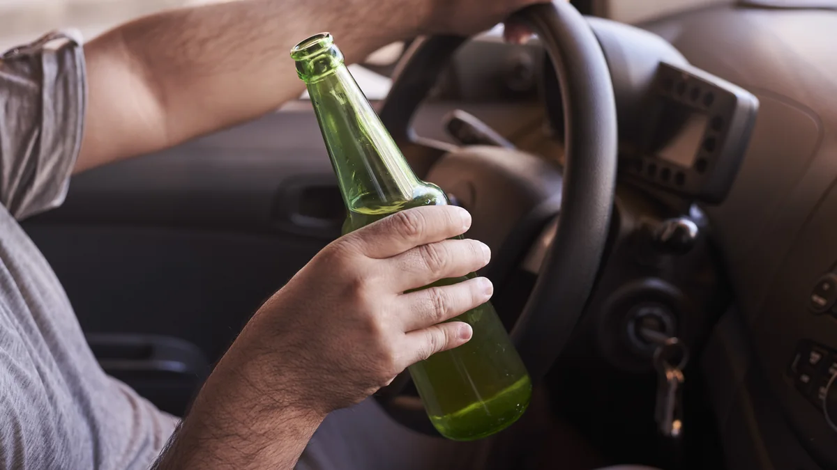Fahrer hält am Steuer eine geöffnete Bierflasche in der Hand