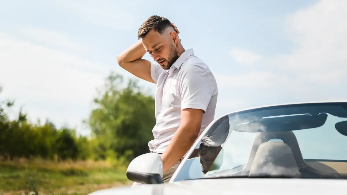 Fahrverbot oder Entzug: Mann steht neben seinem Auto, die Hand im Nacken, Blick nach unten