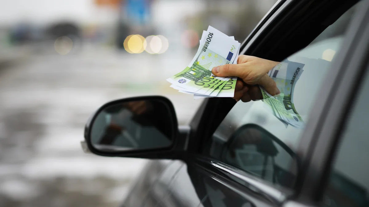 Hand reicht mehrere Hundert-Euro-Scheine aus einem geöffneten Autofenster