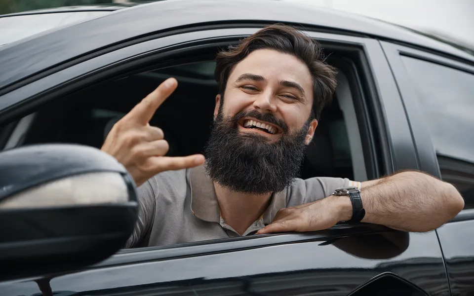 Mann sitzt lachend am Steuer seines Autos, wieder mobil nach dem Führerscheinentzug