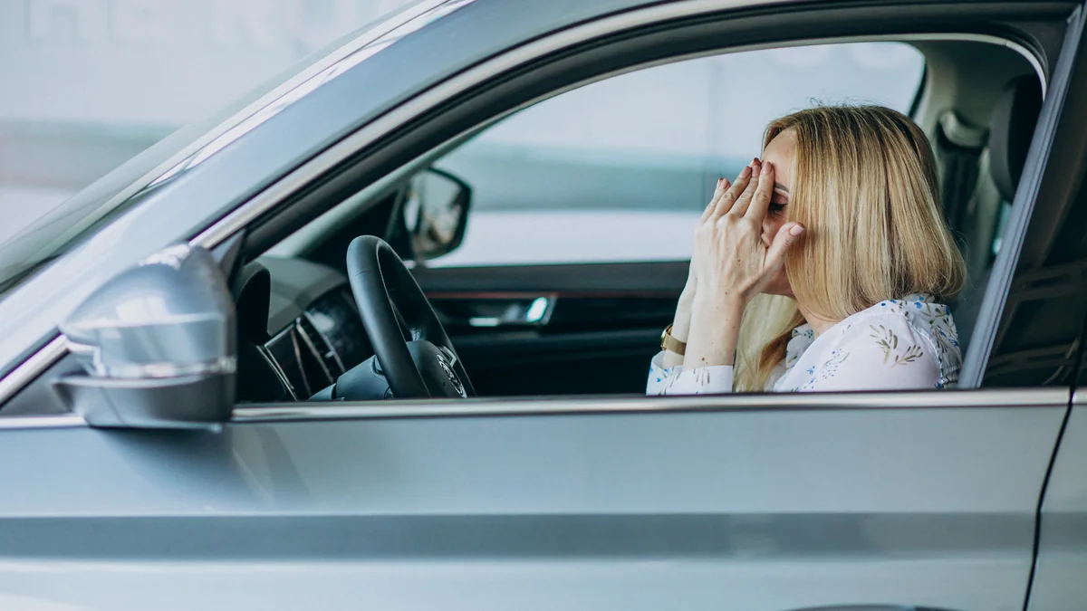 Frau sitzt am Steuer eines Autos und hält sich die Hände vors Gesicht