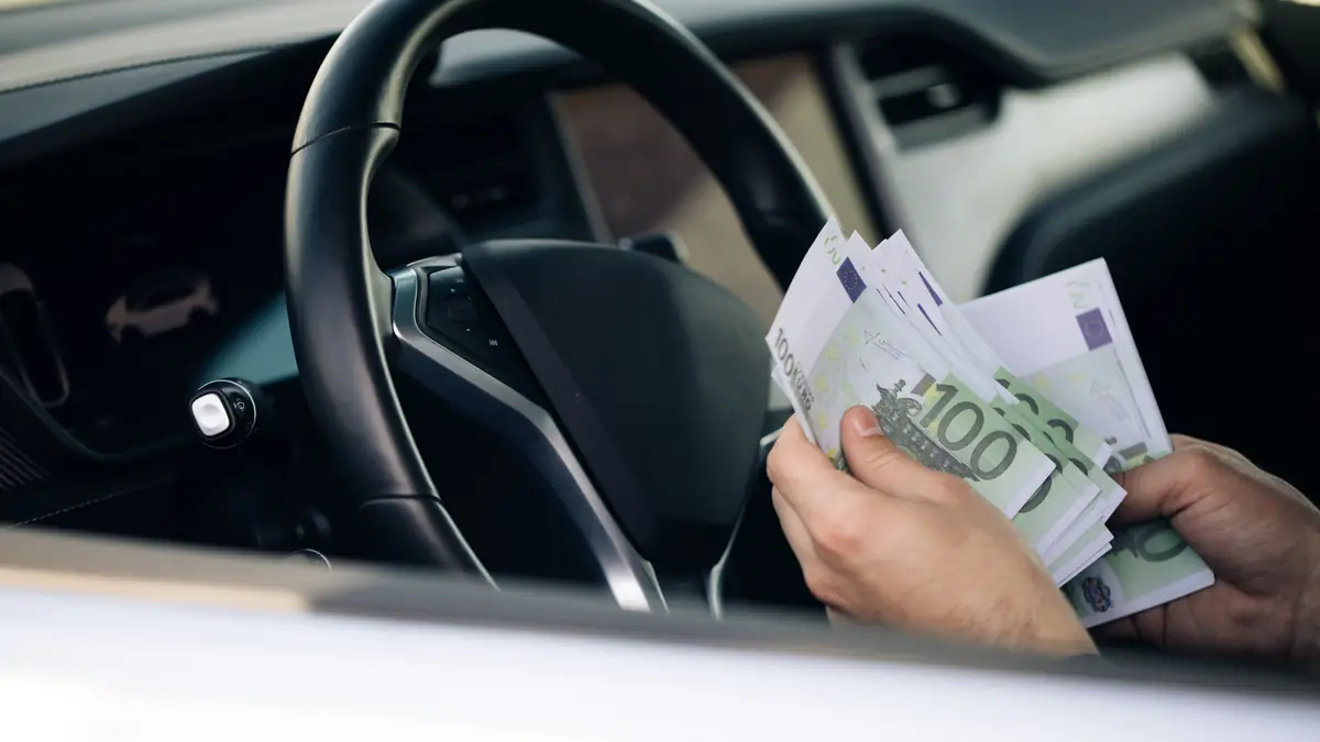 MPU Kosten: Hände zählen Hundert-Euro-Scheine am Lenkrad eines Autos