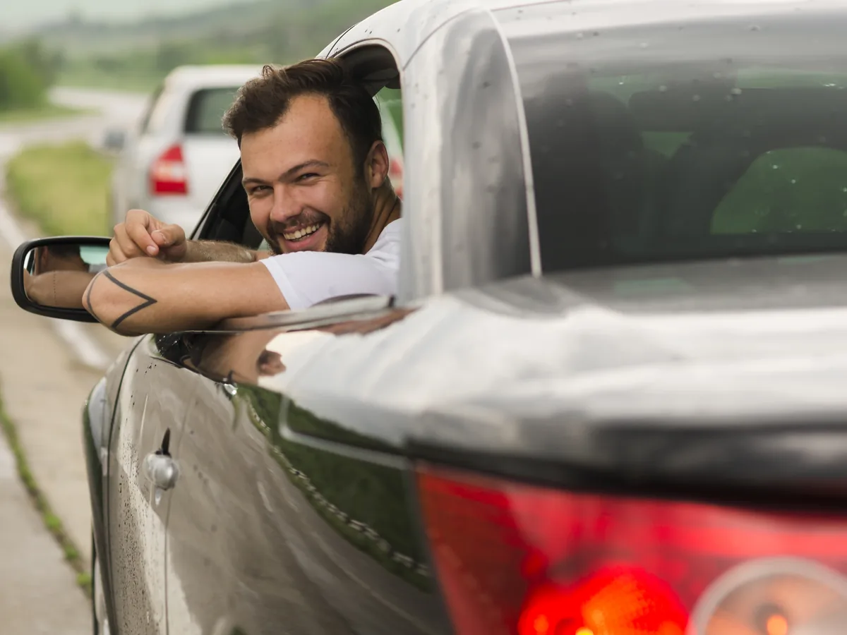 Mann lehnt entspannt aus dem Fenster seines Autos auf einer Landstraße, wieder mobil nach dem Verlust der Fahrerlaubnis